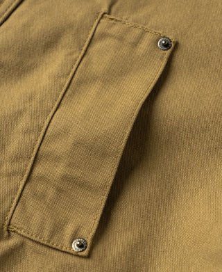 Khaki canvas field jacket sleeve placket close-up with stitched patch and metal button
