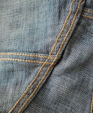 Indigo denim jacket front seam with yellow topstitching and stitched panel edge