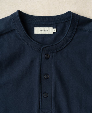 Close-up of a navy blue henley shirt by Time Cracker, featuring a ribbed crew neck, three-button placket, and a white brand label.