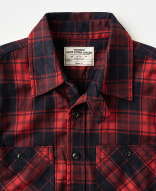 Red and dark navy plaid work shirt close-up with label, button placket, and chest flap pockets