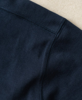 Close-up detail shot of a dark navy blue ribbed knit garment, showing the texture and stitching against a neutral beige background.