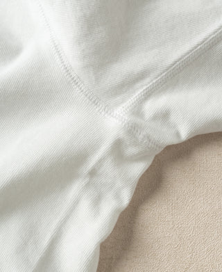Close-up of a white ribbed knit garment, showing the texture and stitching detail against a neutral beige background.