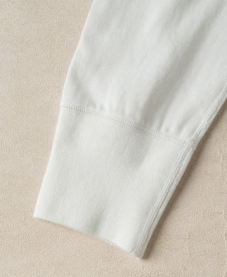 Close-up detail of a light off-white ribbed knit fabric cuff, showing the texture and stitching, laid flat on a neutral beige textured background.