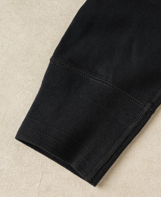 Close-up of a black ribbed knit garment cuff, likely a sweater or sweater vest, laid flat on a textured beige fabric background.