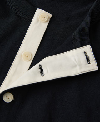 Close-up of a black garment with white trim and buttons on a dark background