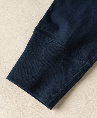 Close-up of a dark navy ribbed knit fabric cuff on a light beige textured background.