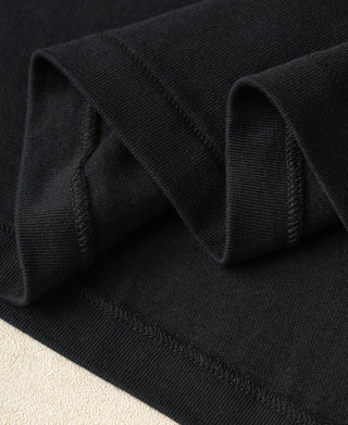 Close-up of a black ribbed knit fabric, likely a t-shirt or sweater, showing the texture and folded edges against a light beige background.