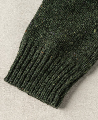 Close-up view of the ribbed sleeve cuff and thick wool knit structure on a dark green fisherman sweater.