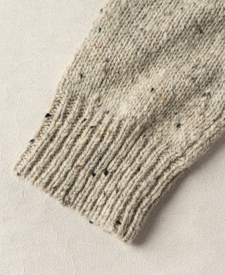 Close-up view of the ribbed sleeve cuff and thick wool knit structure on an ecru fisherman sweater.