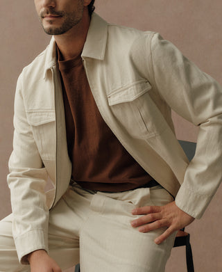 Natural heavyweight cotton Eisenhower jacket with pointed collar and flap chest pockets, worn open.